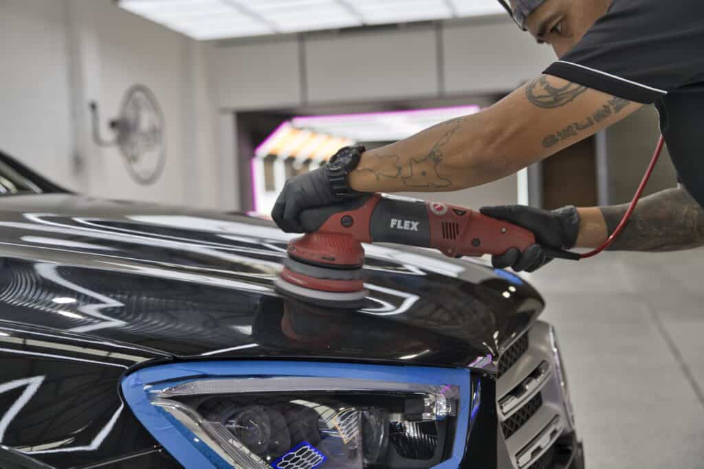 A expert car detailer doing paint correction on the front of a black vehicle