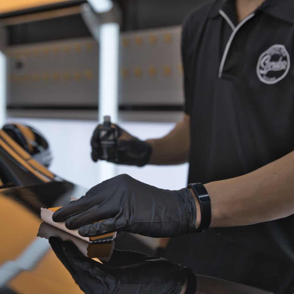 A scrubs team member applying ceramic paint protection to a black vehicle